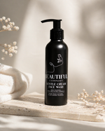 Load image into Gallery viewer, Black bottle of 'Beautiful Company' Gentle Cream Face Wash on a neutral background with flowers.