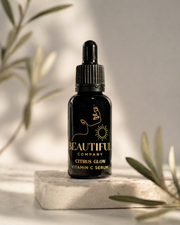 Black serum bottle with dropper labeled 'Beautiful Company Citrus Glow Vitamin C Serum' on a light surface with green leaves in the background.